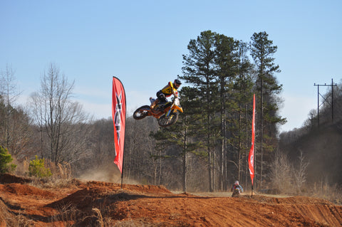 risk racing athlete practicing jumping a dirt bike. The rider sustained consistent throttle up the face of the jump's takeoff and transfers their weight mid air so they can match the angle of the landing with their bike. The rider is wearing risk racing ventilate v2 red, black and yellow gear. As well as risk racing ventilate white/red motocross goggles. The rider is jumping a yellow suzuki rmz250.