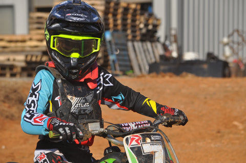 Motocross rider sitting on their kx65 next to a motocross track. wearing the J.A.C. V3 goggles with the mirrored tint tear-off lenses. Wearing the teal/black ventilate v2 gear