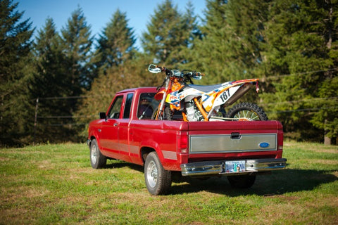 Ktm dirt bike strapped into the truck bed of a for pick up truck. The KTM is strapped in appropriately but using straps causes the forks to compress and this can damage fork seals over long periods of time.