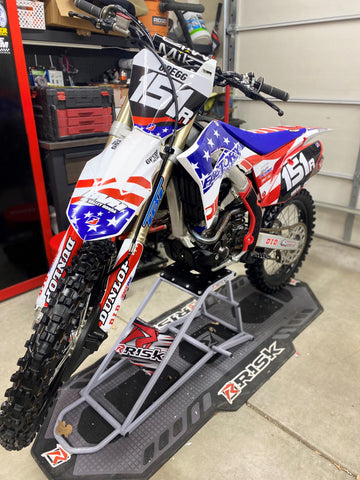 Dirt bike resting with it's wheels off the ground with RISK Racings Ride-On-Lift  Stand. On top of a risk racing pit mat.