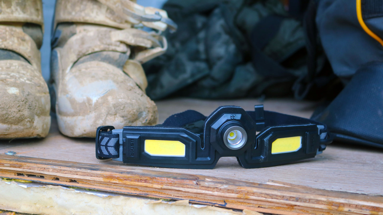 Close up lifestyle image of a Headlamp 3.0 sitting near a pair of muddy motocross boots.