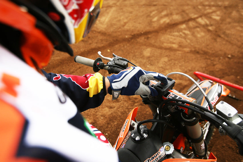 Démarrage à distance Holeshot Gate. Photo par-dessus l'épaule d'un coureur MX appuyant sur le bouton monté sur son guidon