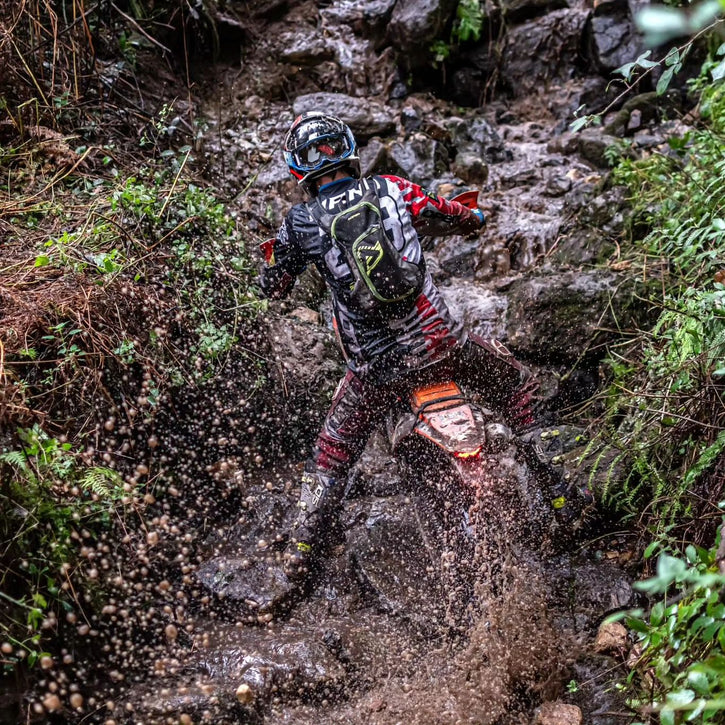 Enduro Racer grimpant une colline très raide, humide et rocheuse. Son pneu de pneu plews ne fait que jeter de l'eau sale