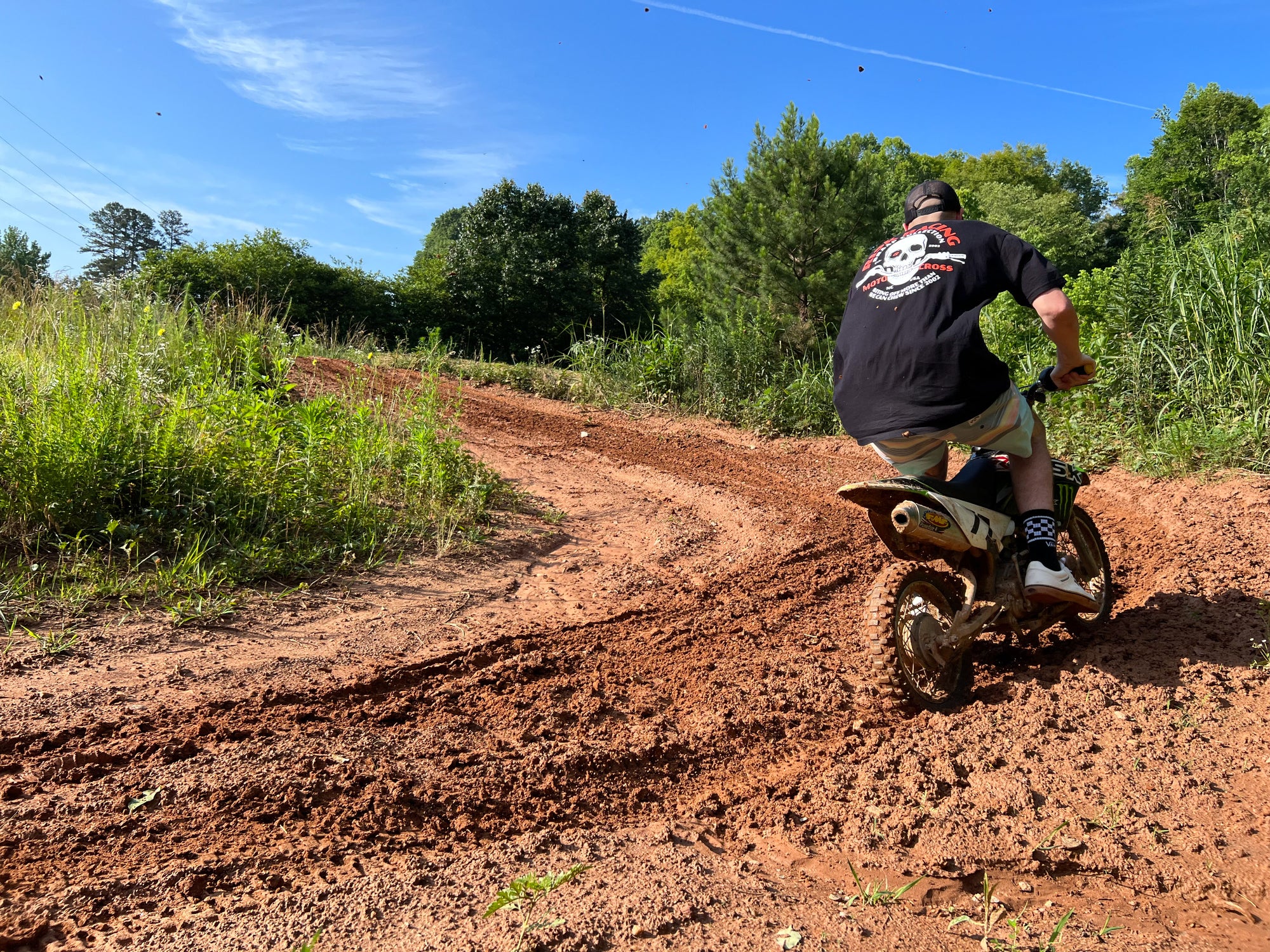 Un hombre montando una pit bike con una camiseta negra de "Bones y barras"