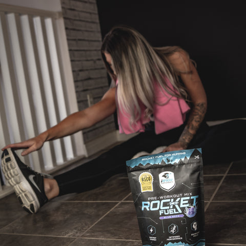 Atleta de motocross estirándose antes de un entrenamiento. Tienen una bolsa de preentrenamiento Rocket Fuel de iRide Supplement frente a ellos para mezclarlo con un poco de agua y obtener un impulso de energía para un entrenamiento más efectivo.