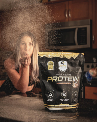 Woman in kitchen blowing iRide chocolate protein powder towards the camera with a bag of the iRide chocolate lean whey protein powder