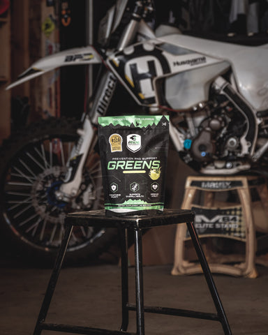 RISK Racing iRide supplements sour apple flavored greens sitting on a motocross stand in front of a motocross bike