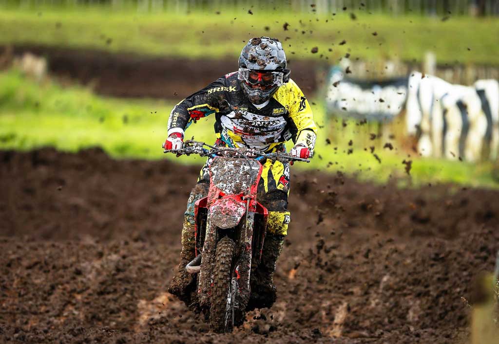 Motocross racer coming straight at camera through heavy mud wearing black and yellow Risk Racing moto gear