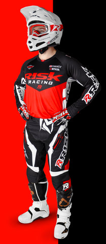 person standing in risk racings red/black ventilate v2 mix-n-match series gear with the v2 white/red goggles in a white helmet and white boots. The person is standing with their hands on their hips.