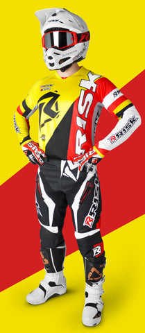 person standing in risk racings red/yellow ventilate v2 mix-n-match series gear with the v2 red/black goggles in a white helmet and white boots. The person is standing with their hands on their hips.