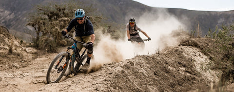 Two mountain bikers descending down a rocky and dusty slope. Grips have to be durable for terrain like this. They get pushed to the limit and have to be able to resist crashes when things don't go as planned.