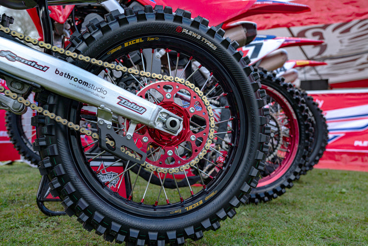 Mehrere Motocross -Motorräder in einer Linie mit einer Nahaufnahme des hinteren Reifens des 1., der die Plews -Reifen mx2 leitender GP hervorhebt