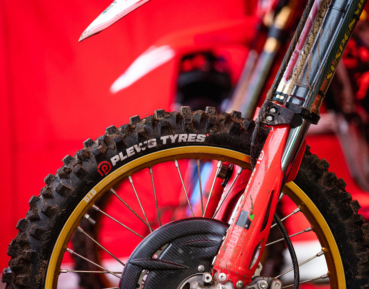 Close up of a motocross bike's front tire and front forks. Plews Tyres logo on the side of the front tire.