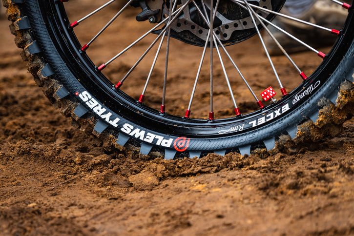 Super close up on a rear dirt bike tire with the Plews Tyres logo prominently displayed in white against the black rubber.