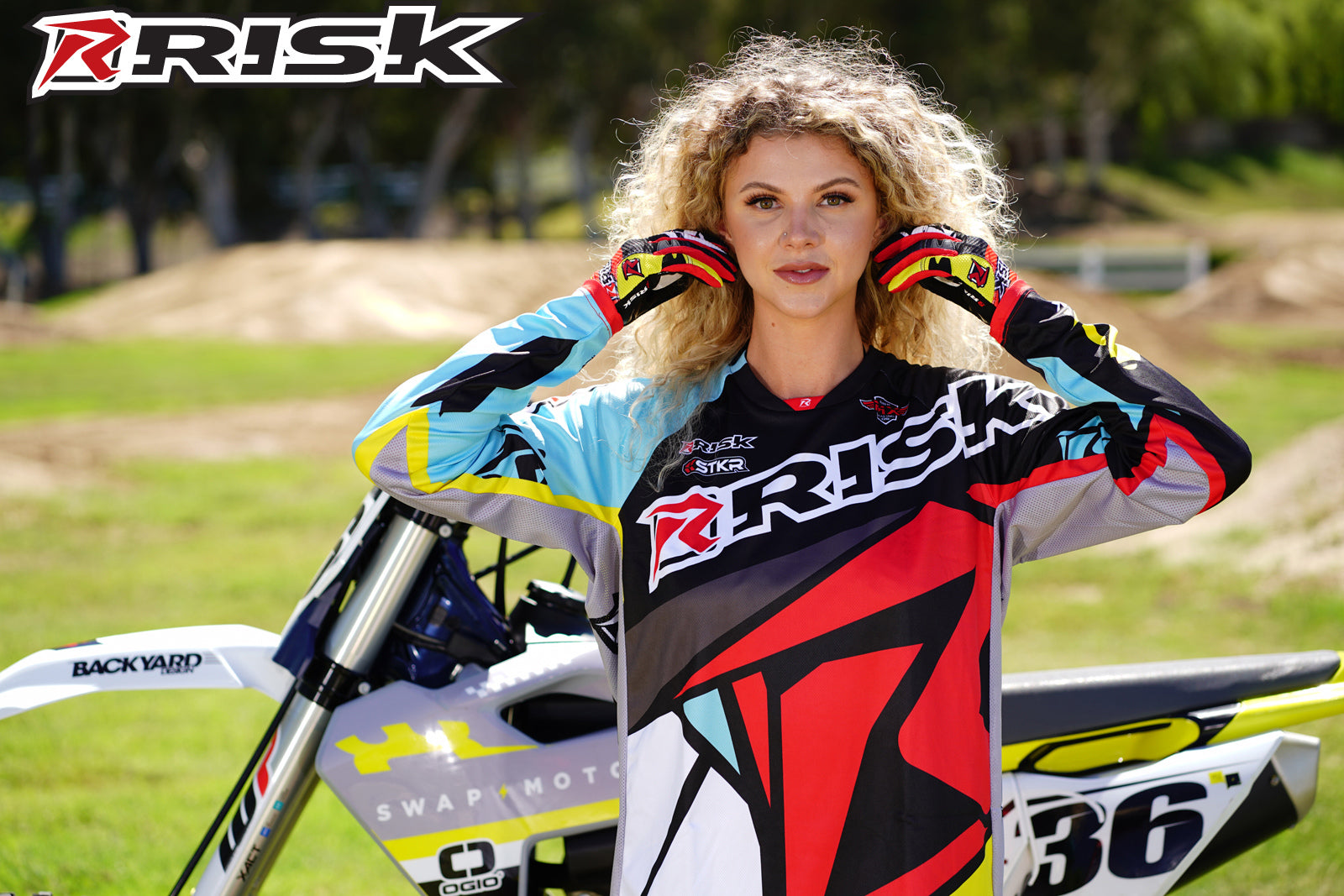 September's Risk Racing Moto Model Denna Lynn posing in various bikinis & Risk Racing Jerseys next to a dirt bike that's sitting on a Risk Racing ATS stand - Pose #12