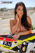 Risk Racing's March Moto Model Amber Juliana wearing a bikini top standing behind a motocross bike resting one forearm on the seat and gently touching her neck with the other hand - close up shot - white fenced off MX track in background