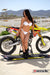 Risk Racing's March Moto Model Amber Juliana wearing a white bikini standing in front of a motocross bike sitting on an ATS stand by Risk Racing