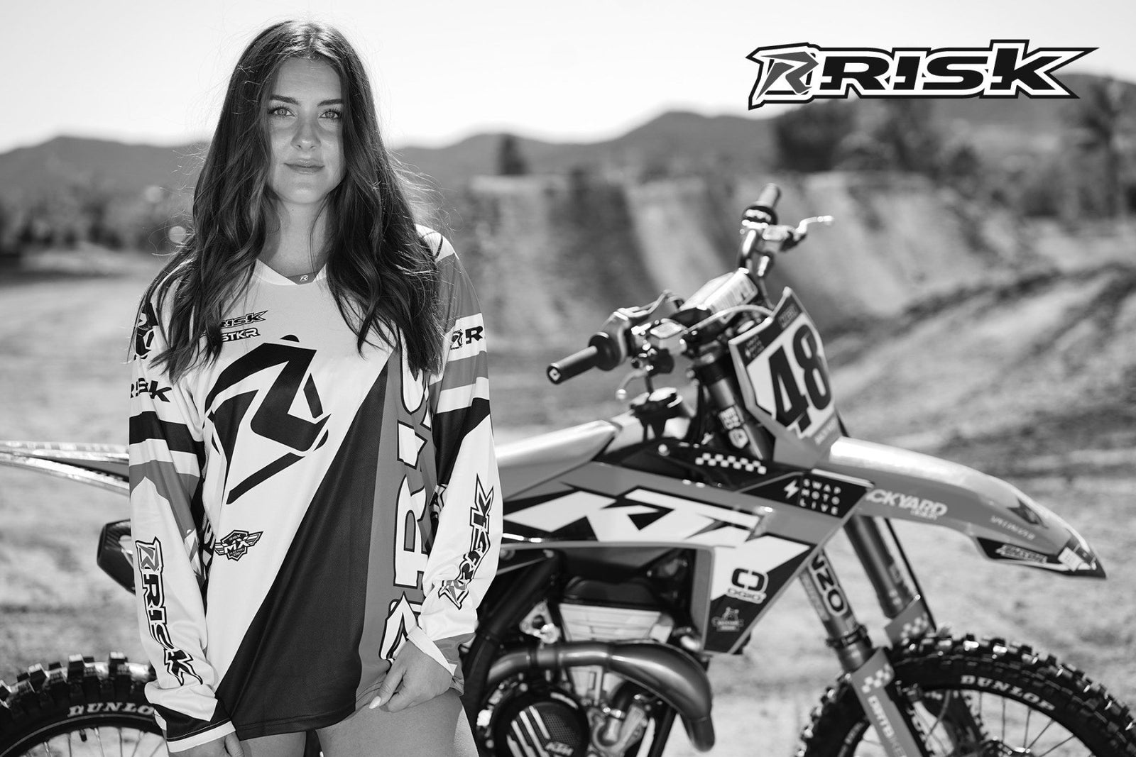 October's Risk Racing Moto Model Dani Hamilton posing in various bikinis and Risk Racing Jerseys next to a dirt bike that's sitting on a Risk Racing ATS stand - Pose #12