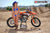 October's Risk Racing Moto Model Dani Hamilton posing in various bikinis and Risk Racing Jerseys next to a dirt bike that's sitting on a Risk Racing ATS stand - Pose #14
