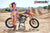 October's Risk Racing Moto Model Dani Hamilton posing in various bikinis and Risk Racing Jerseys next to a dirt bike that's sitting on a Risk Racing ATS stand - Pose #31
