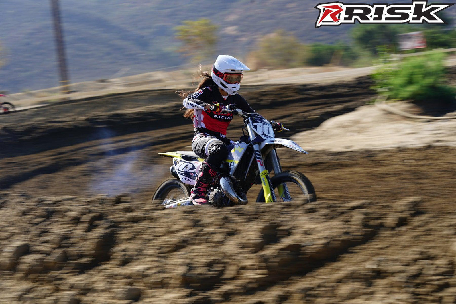 La modelo de moto de Risk Racing de octubre, Jessica Victorino, posa con varios bikinis y camisetas de Risk Racing junto a una moto de cross que está sentada en un soporte RR1-Ride-On de Risk Racing - Pose n.° 18