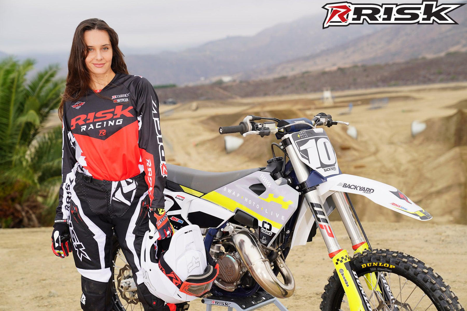 La modelo de moto de Risk Racing de octubre, Jessica Victorino, posa con varios bikinis y camisetas de Risk Racing junto a una moto de cross que está sentada en un soporte de Risk Racing RR1-Ride-On - Pose n.° 22