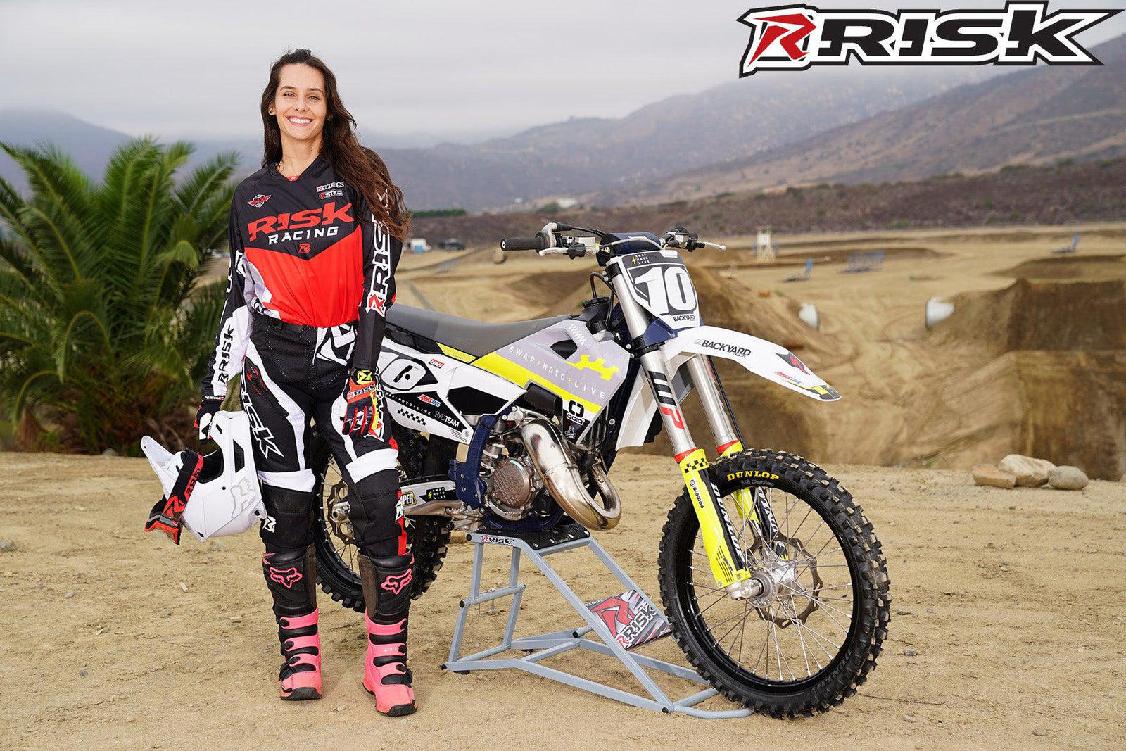 La modelo de moto de Risk Racing de octubre, Jessica Victorino, posa con varios bikinis y camisetas de Risk Racing junto a una moto de cross que está sentada en un soporte RR1-Ride-On de Risk Racing - Pose n.° 2