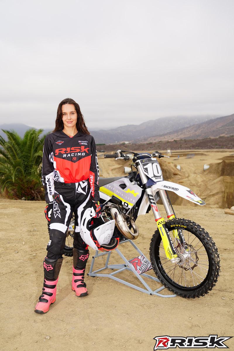 La modelo de moto de Risk Racing de octubre, Jessica Victorino, posa con varios bikinis y camisetas de Risk Racing junto a una moto de cross que está sentada en un soporte RR1-Ride-On de Risk Racing - Pose n.° 4