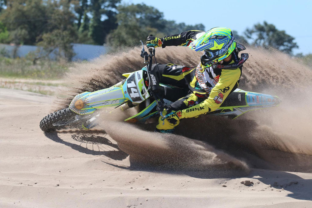 Risk Racing Pro Rider riding a berm of sand through a corner on a motocross dirt bike sand flying