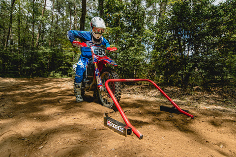 motocross racer practicing their starts on the risk racing holeshot practice starting gate. The racers body is positioned so they are sitting in a neutral position while leaning forward with the elbows locked. This allows the rider to keep enough weitght over the rear tire so they can accelerate but not so much weight over the rear of the motorcycle that the bike flips over or gets out of control as the rider accelerates.