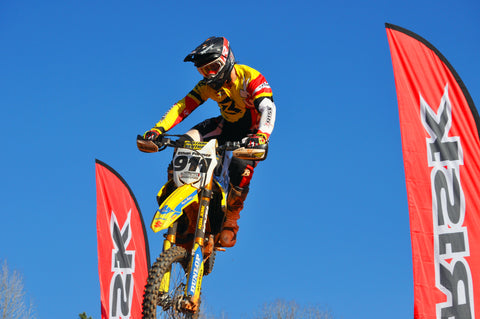 Motocross rider jumping between two risk racing feather flags. Wearing risk racings ne ventilate v2 mix-n-match motocross gear
