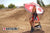 Risk Racing's June Moto Model Rochelle Roche wearing a Risk Racing Factory Pit Dry-Fit Shirt and black boots sitting on an ATS Stand and holding a Factory Umbrella. MX track in the background.