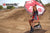 Risk Racing's June Moto Model Rochelle Roche wearing a Risk Racing Factory Pit Dry-Fit Shirt and black boots sitting on an ATS Stand and holding a Factory Umbrella. MX track in the background.