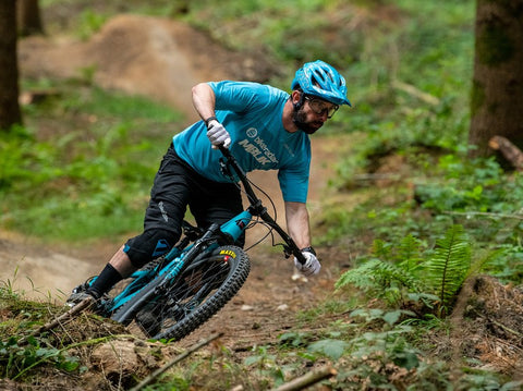 Mountain biker descending down a curvy single track. The rider is rounding a berm holding tightly onto the grips so they can keep control of the bike.