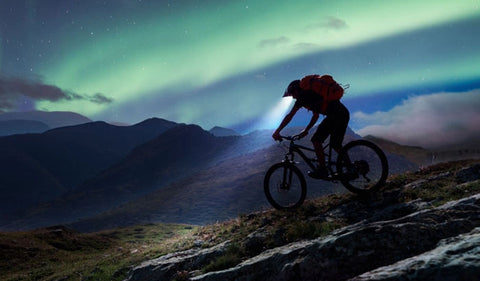 Mountain biker deescending at night with a headlamp attached to their helmet.