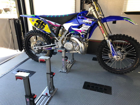 Yamaha YZ250 secured with the risk racing's lock-n-load pro inside of an enclosed trailer. Next to the secured yz 250 is another lock-n-load pro unit that is currently empty.