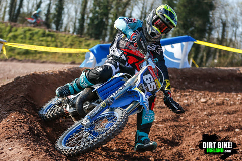 Risk racing athlete turning their blue TM125 motocross bike in a berm on a rocky motocross track in red ,teal, and yellow risk racing ventilate v2 mx gear.