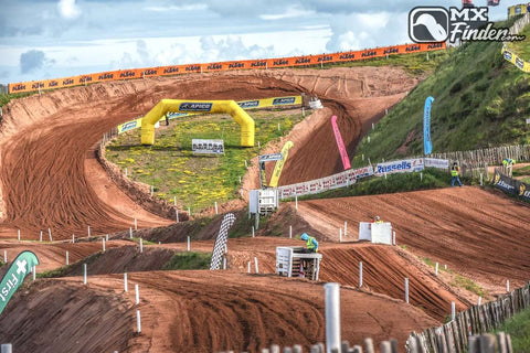 Motocross track with massive elevation changes, jumps, and berms. Track tape and ribbons set up alongside the track.