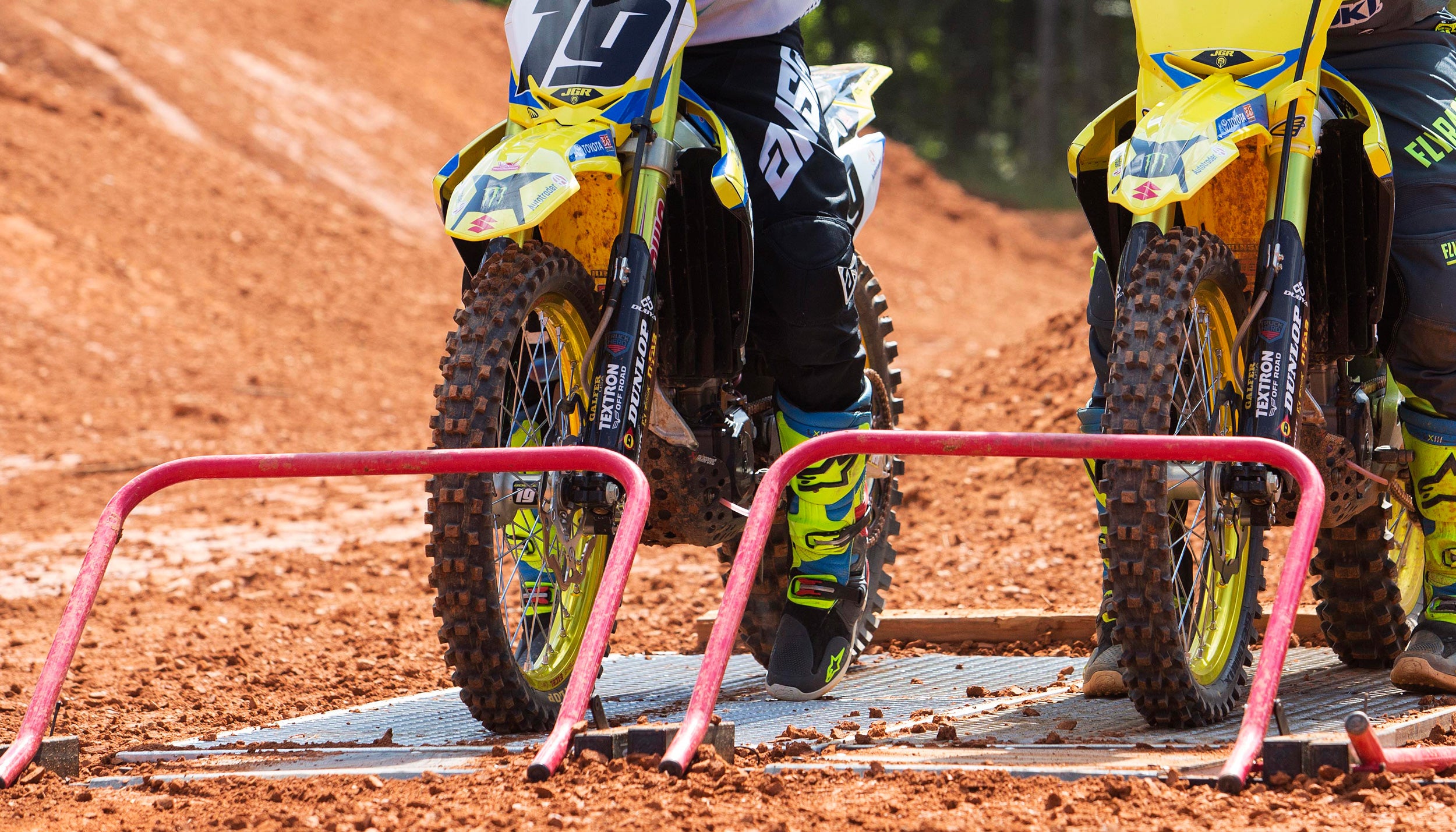 Primer plano de dos motos de motocross esperando a que caigan las puertas de la carrera Holeshot. Producto de Risk Racing. Pista borrosa en el fondo.