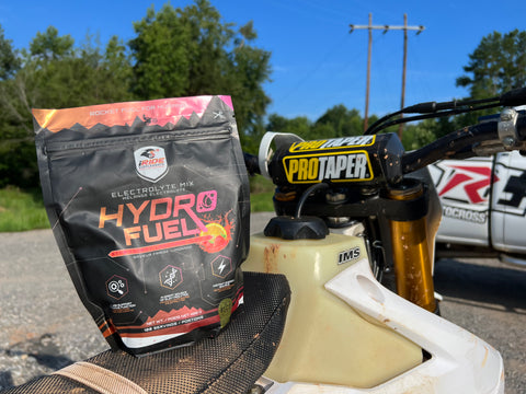 iRide Hydro Fuel strawberry lemonade bag sitting on the seat of a dirt bike in font of the risk racing truck