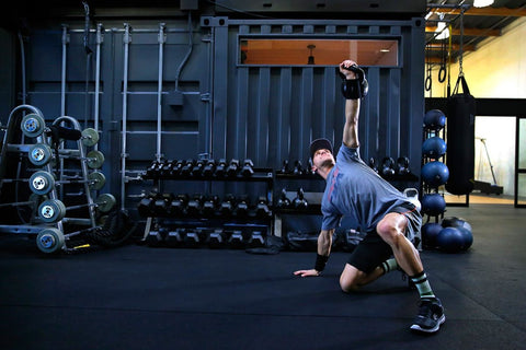 Ken Roczen, pilote de motocross professionnel, fait des exercices de renforcement de base dans une salle de sport avec des haltères et des haltères en arrière-plan.