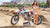 Wide Schuss des Februar-Moto-Modells Alliyah in einem Bikini, der vor einem KTM-Schmutzrad auf einem Risiko-Rennsport-ATS-MX-Stand an einem MX-Track mit Bergen im Hintergrund steht. Ihr rechter Arm, der auf den Griffstäben ruht.