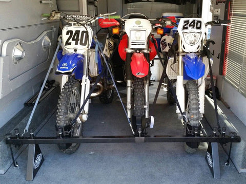 three motorcycles loaded into a trailer using a combination of wheel chocks and several sets of tie down straps which cause a disorganized and messy set up