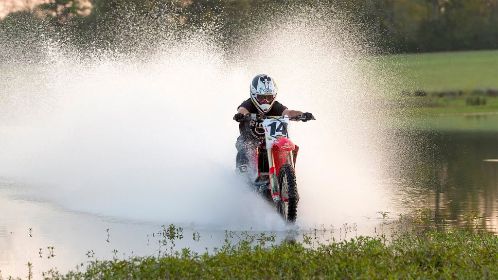 mx number 14 exiting a lake onto the shore surrounded by white water splash