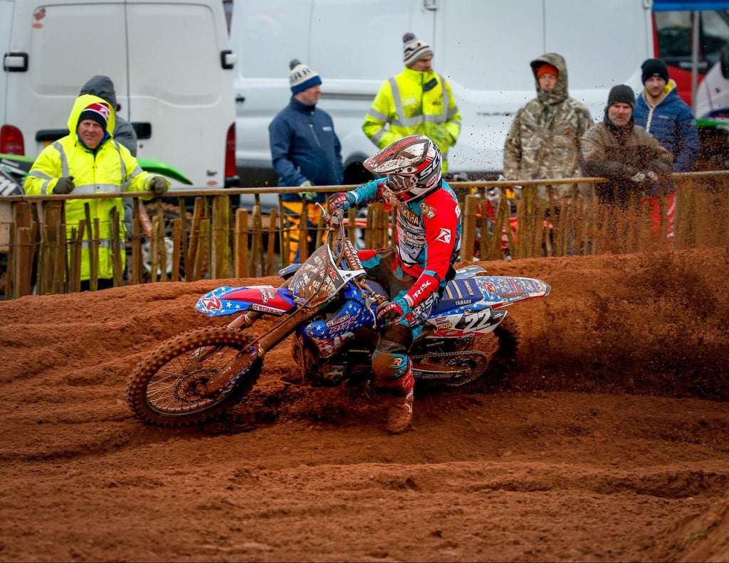 mx number 22 Risk Racing pro rider (in full Risk Racing gear including jersey, pants, and gloves) taking a very muddy corner on a rainy track day