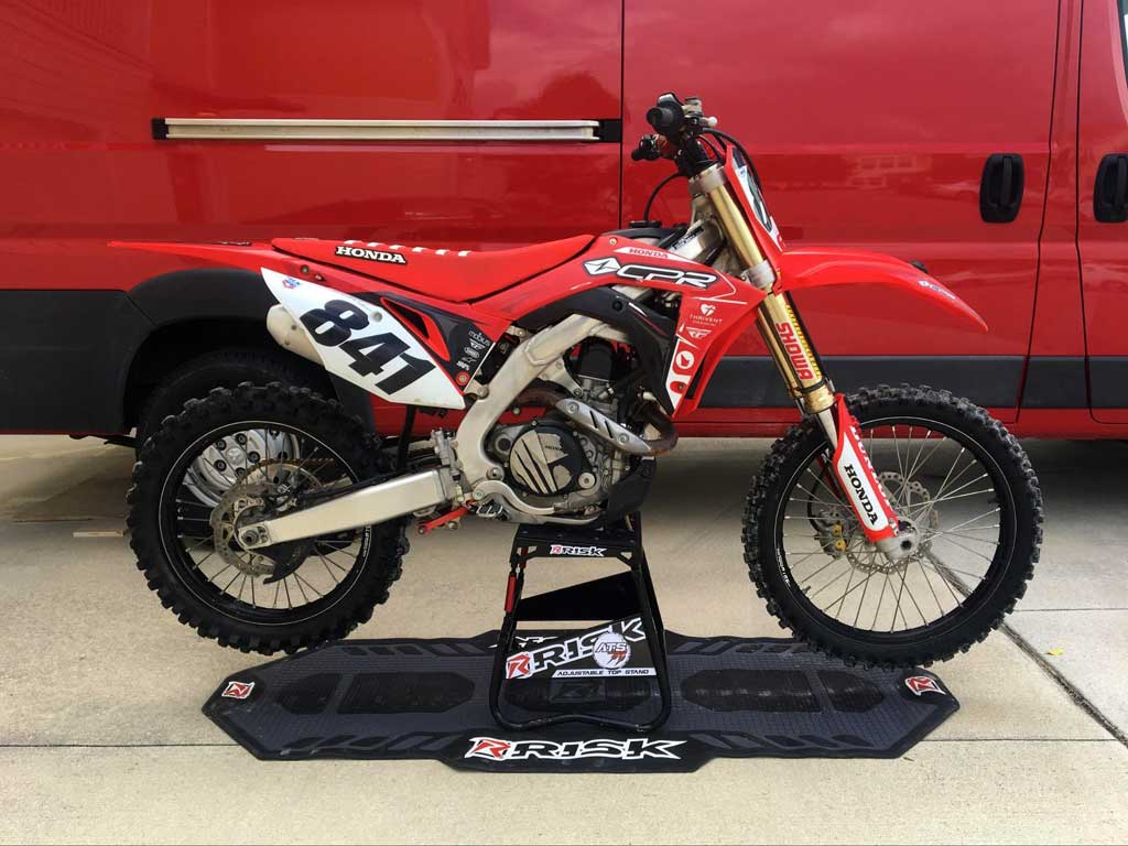 num 841 red honda Dirt Bike sitzt auf einem ATS-Ständer und einer Boxenmatte von Risk Racing Red Motovan im Hintergrund