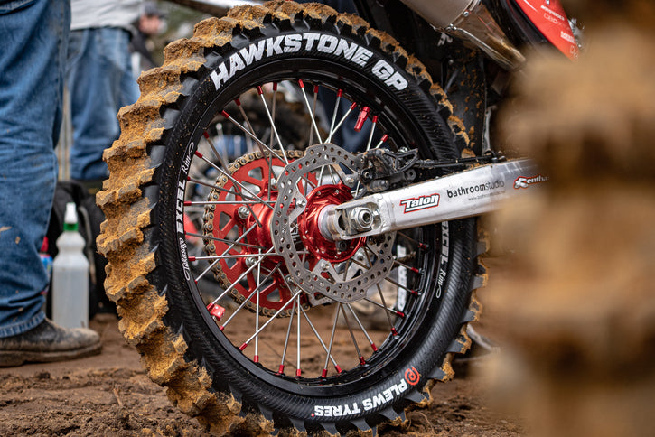 Close up on a dirt bike rear tire and swing arm. Brand new HAWKSTONE GP from Plews Tyres with a clean sidewall and dirty paddles.