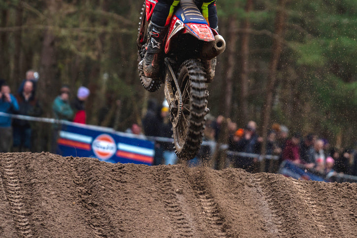 Close up of a motocross rider just leaving a muddy mx jump. back tire tread is very visible on the MX1 Hawkstone GP by Plews Tyres.