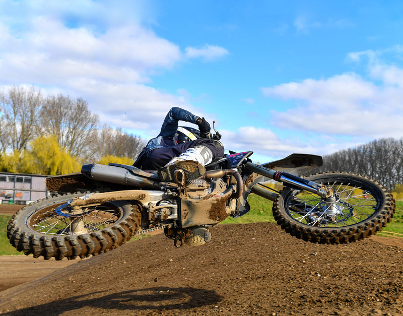 motocross racer whipping super low over a jump and very horizontal. bottom of the bike towards camera really showing us the plews tires.