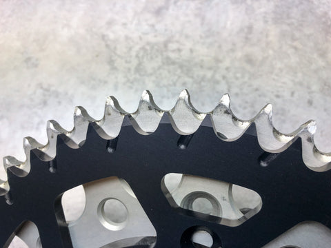 Old sprocket being compared to a new sprocket. The old sprocket is what they call "shark toothed" which means use has worn the teeth of the sprocket to be cupped out at the bottom of the tooth. 